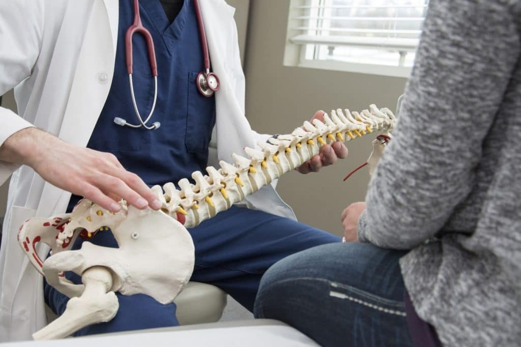orthopaedic surgeon holding a model spine talking to a patient