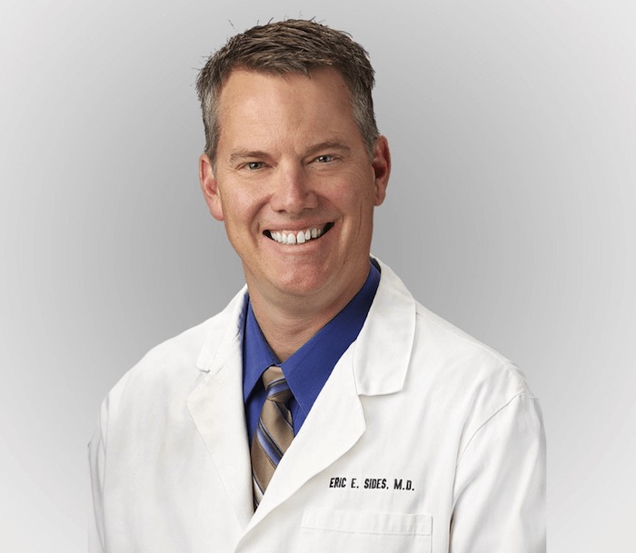 A professional profile picture of Dr. Eric Sides in his white surgical scrubs. 